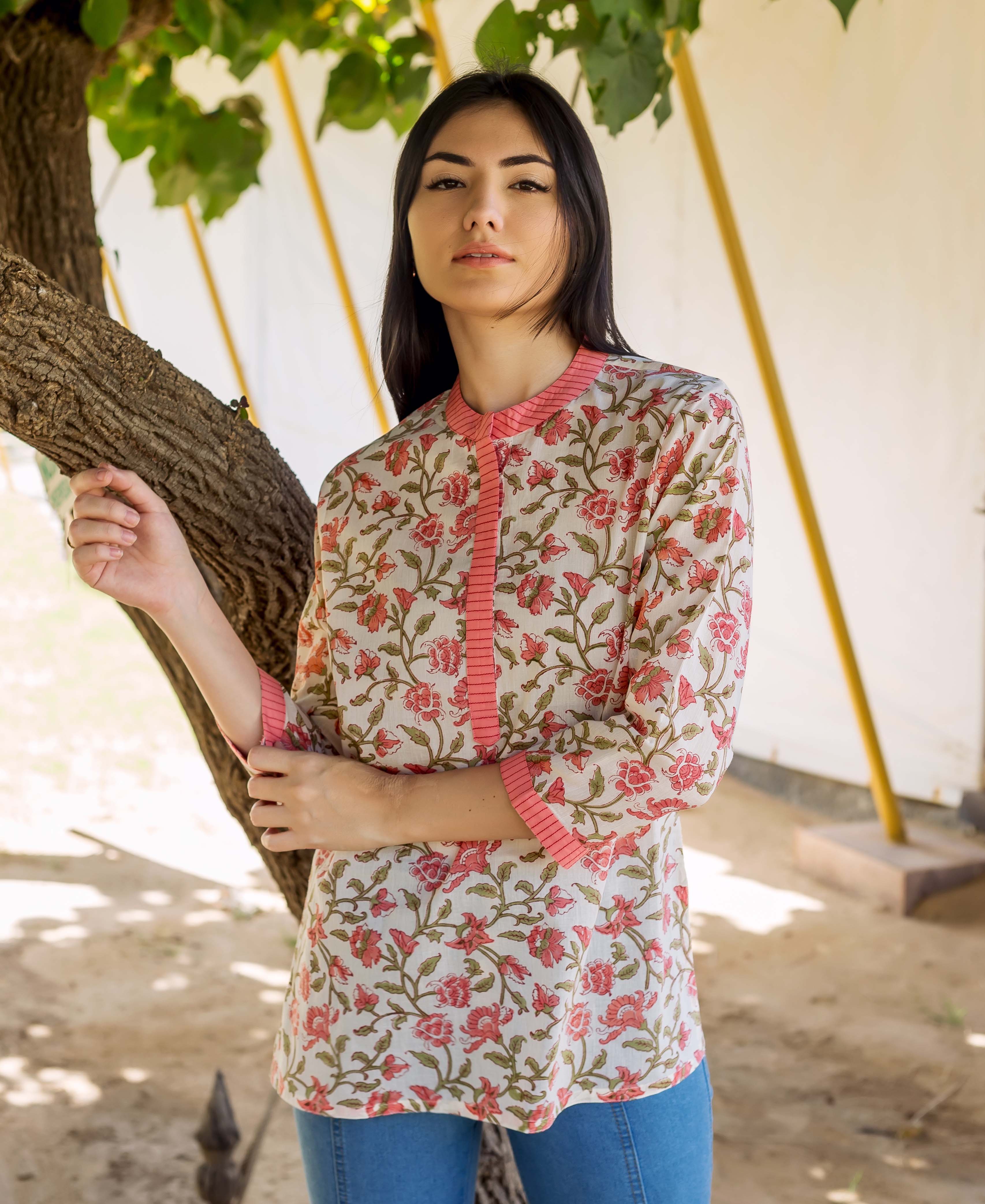 A woman wearing a peach floral printed top with a tree trunk in the background.