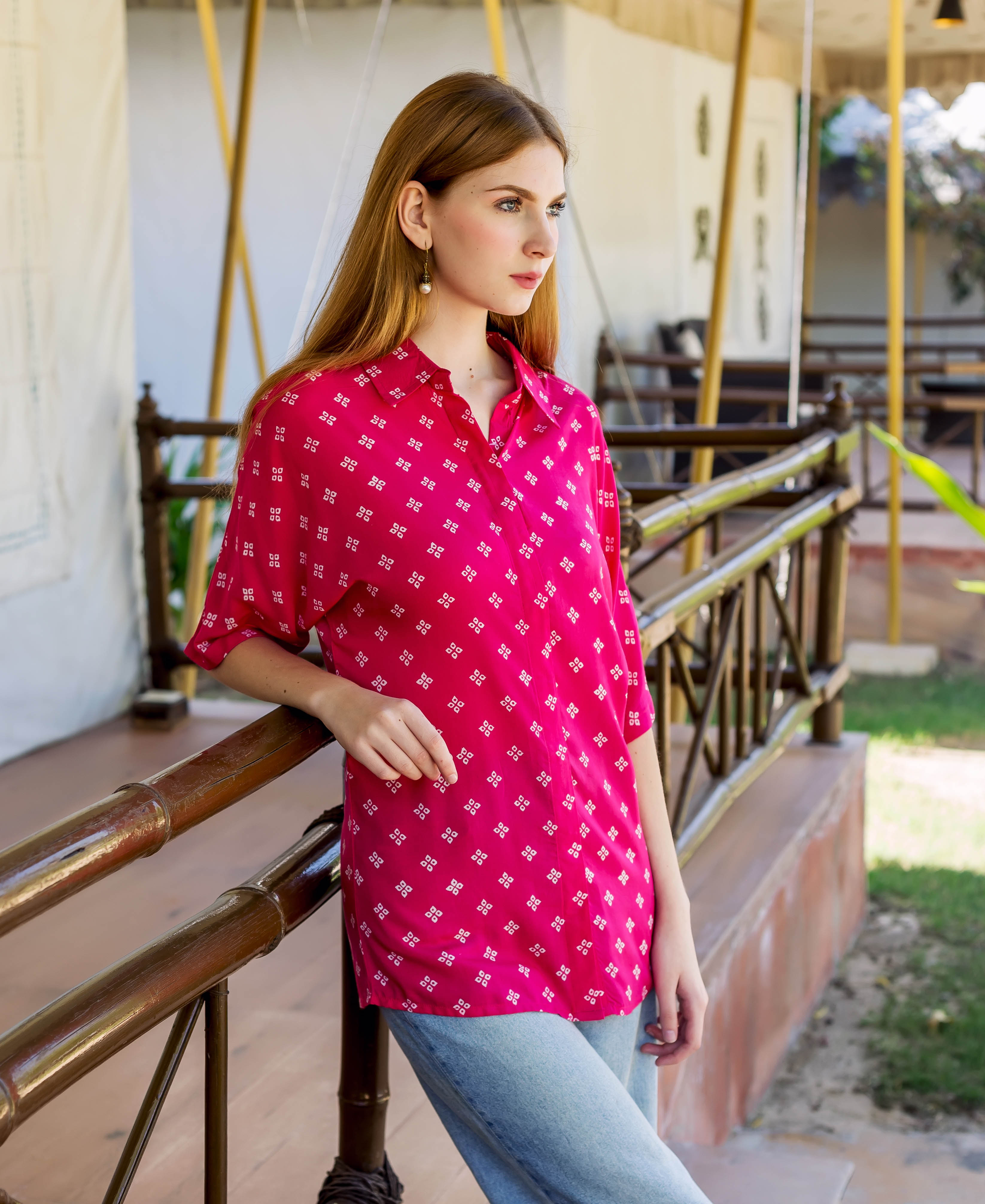 Magenta bandhej printed button-down shirt with white square patterns on a woman leaning on railing.