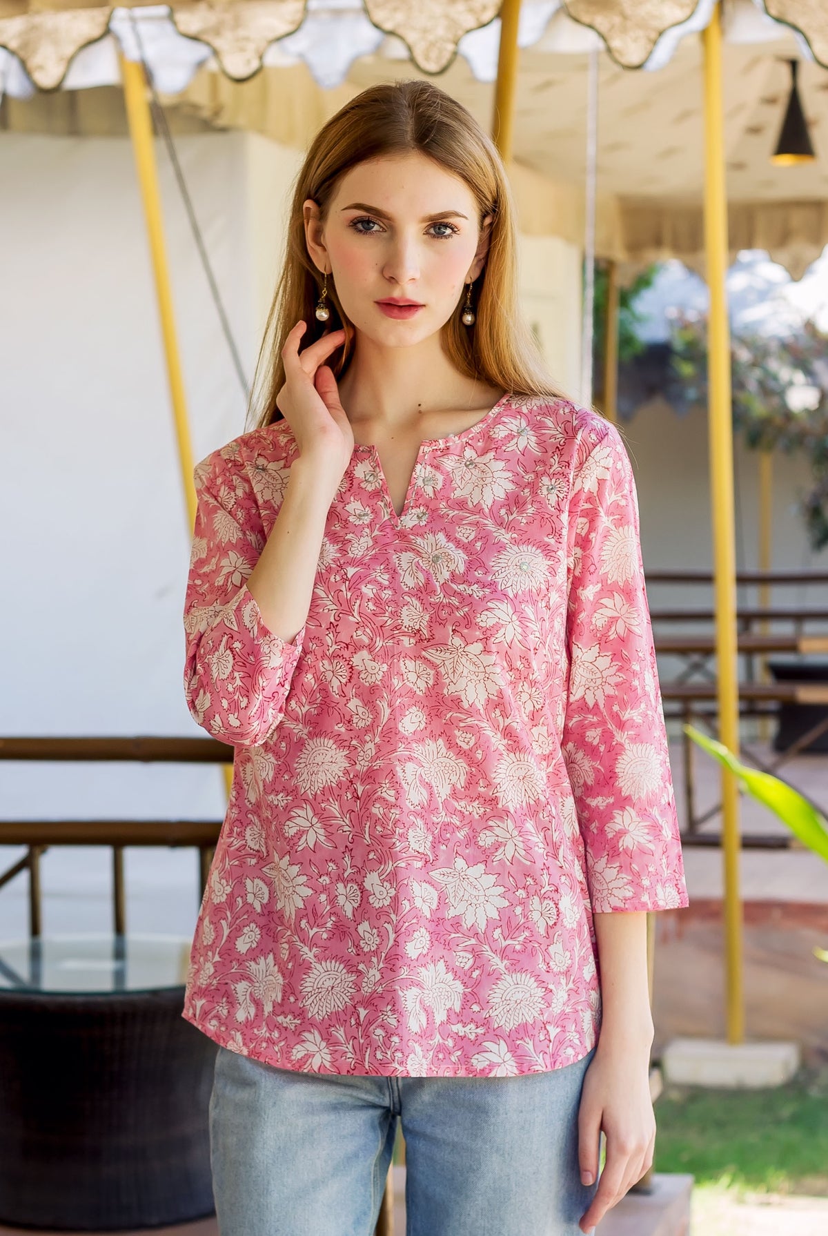 Front-facing model wearing a pink V-neck top with white floral block print.