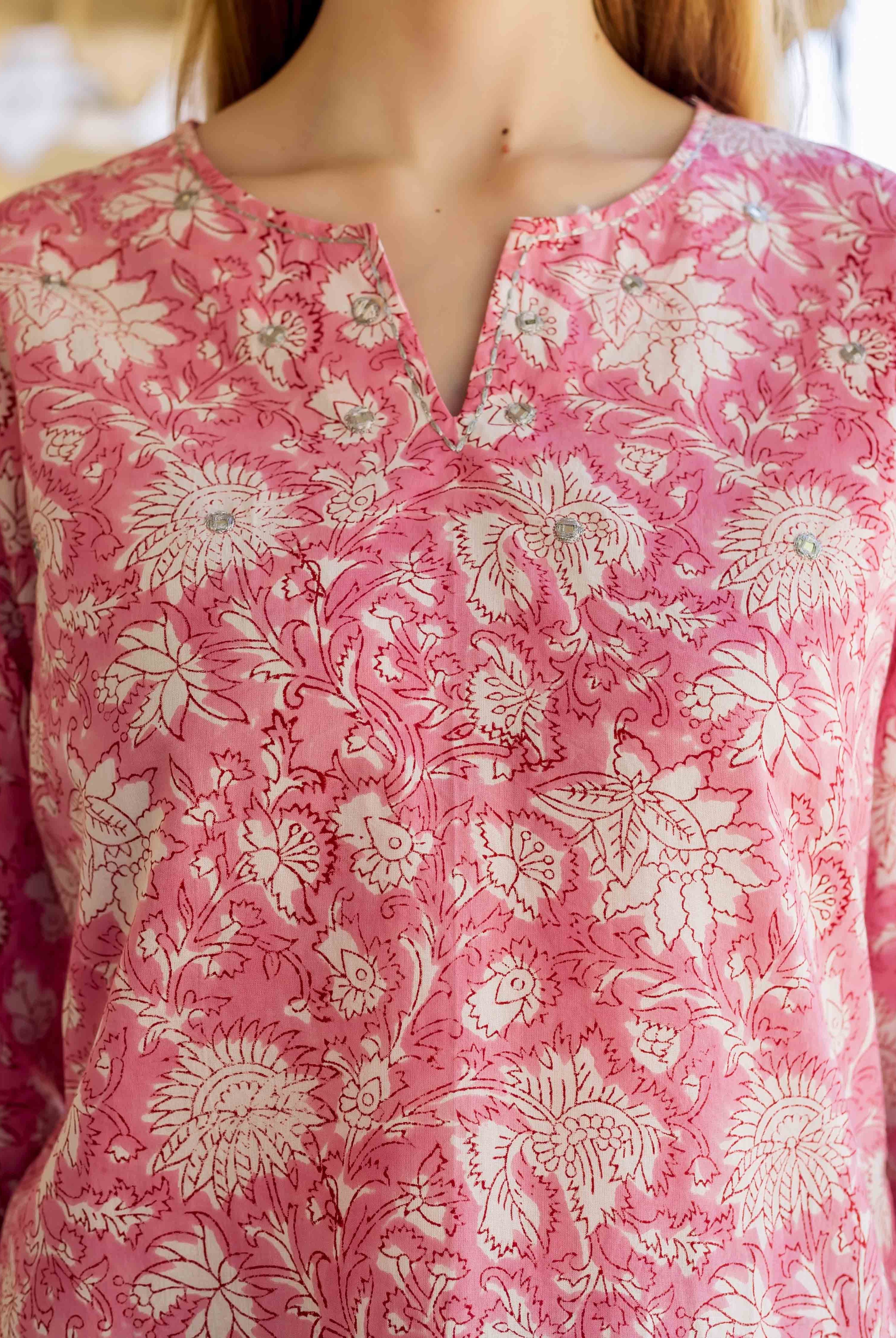 Model wears pink hand-block-printed floral top with notched V-neck and metallic details.
