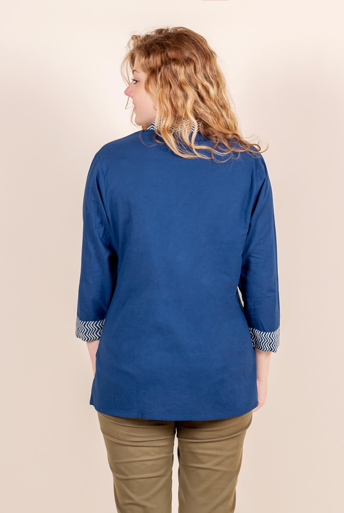 Back view of model wearing blue ethnic top with chevron print on cuffs and collar.