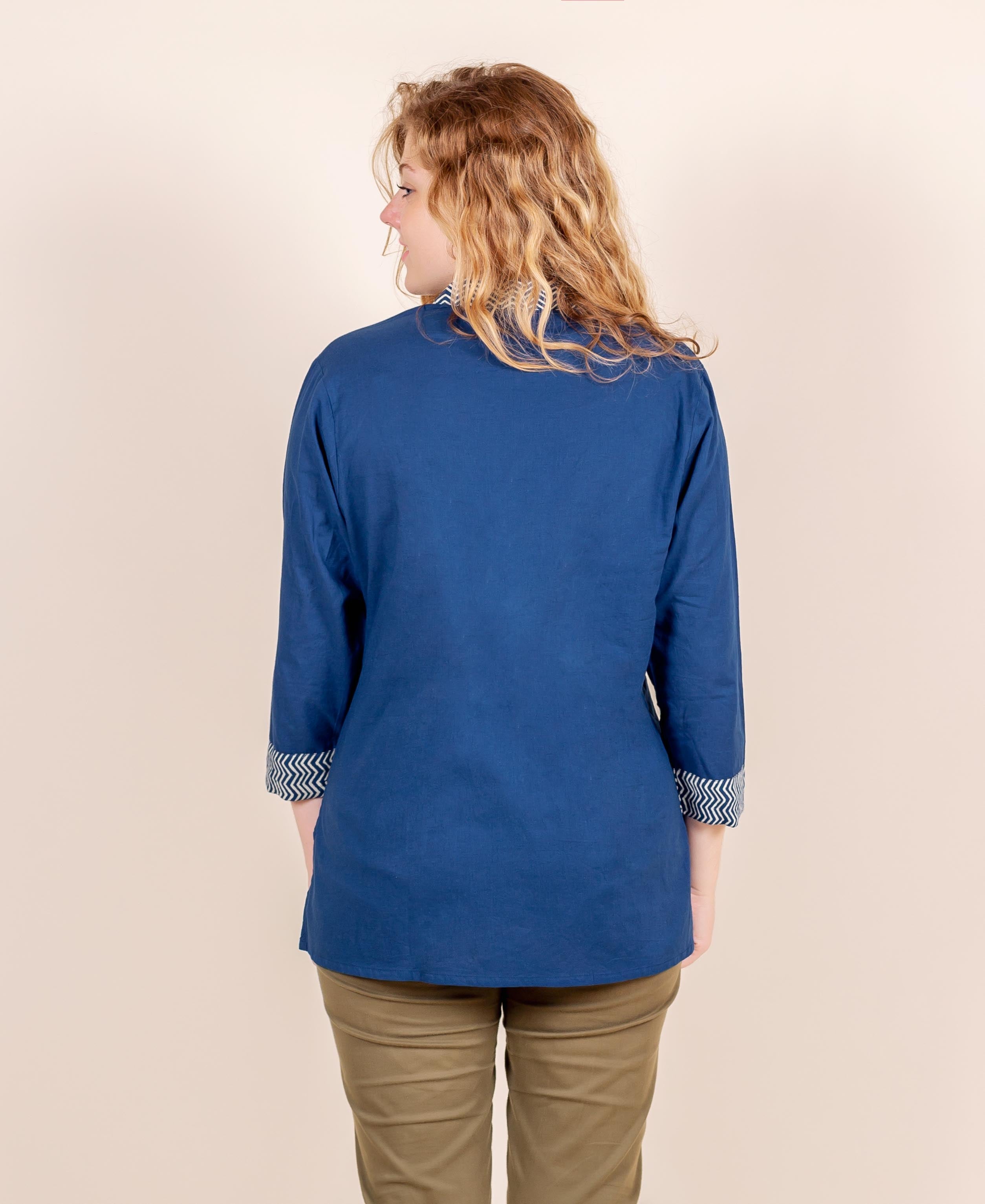 Back view of model wearing blue ethnic top with chevron print on cuffs and collar.