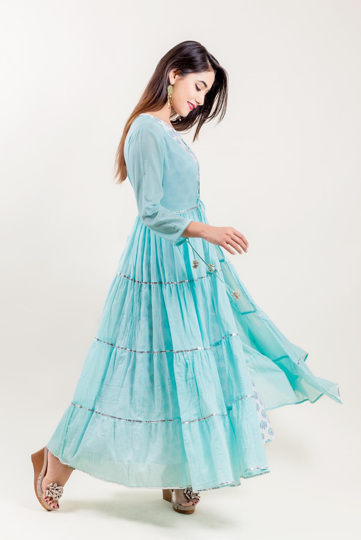 Side view of a model wearing an aqua tiered Indo Western dress with silver accents.