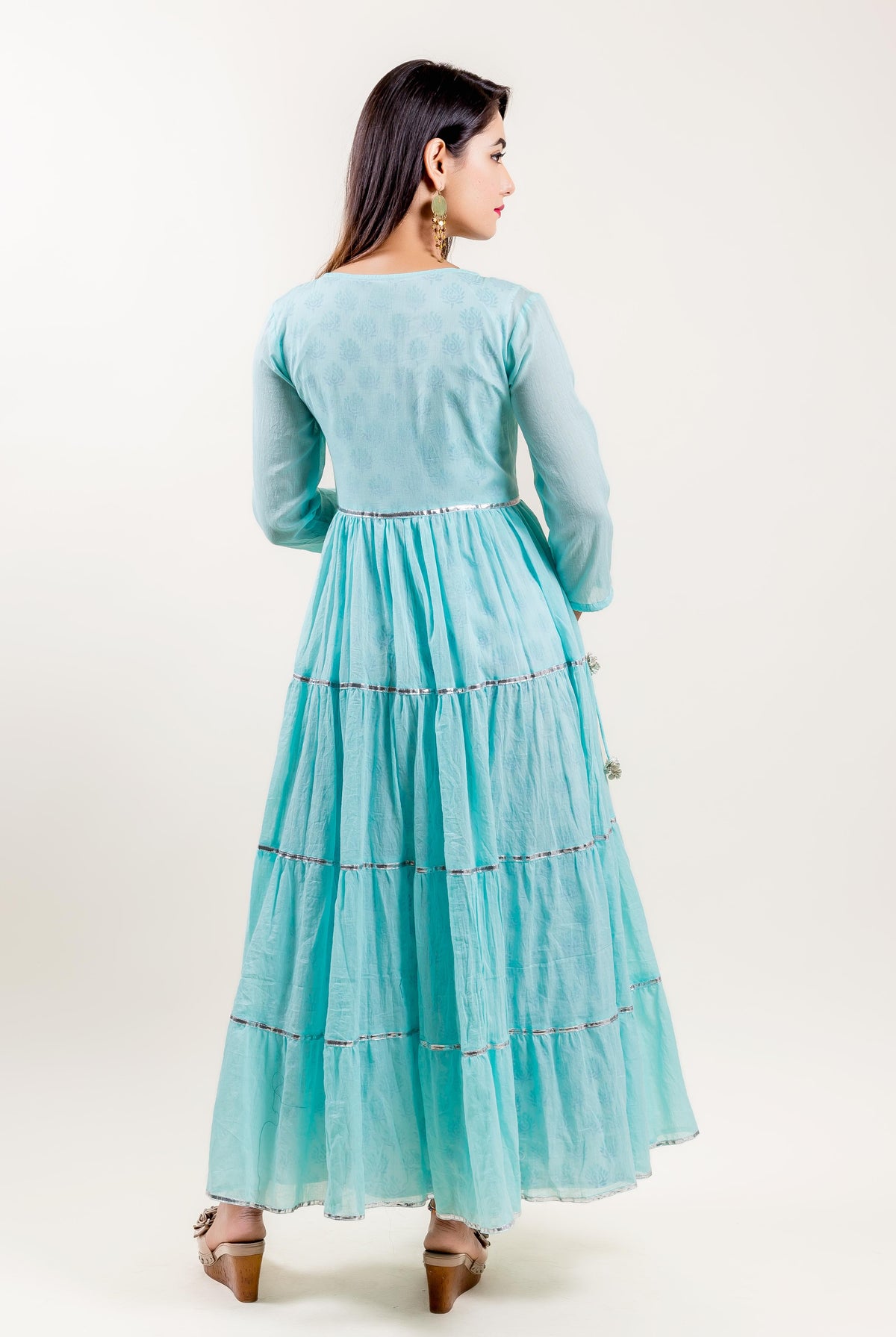 Back view of model wearing full-length aqua tiered dress with subtle print and silver trim.