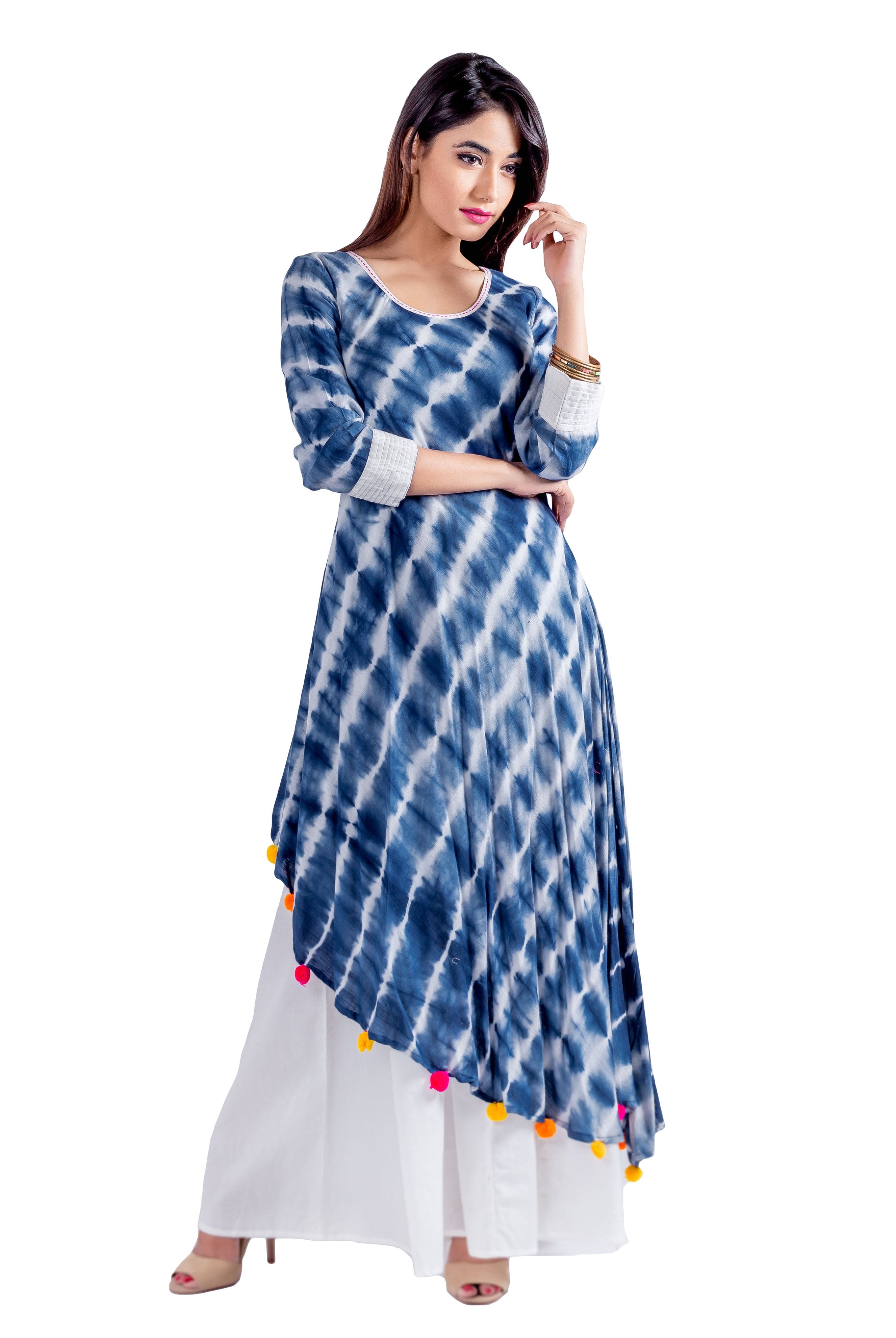 Model wears blue and white tie-dye asymmetric kurta with colorful pom-poms over white palazzo pants.