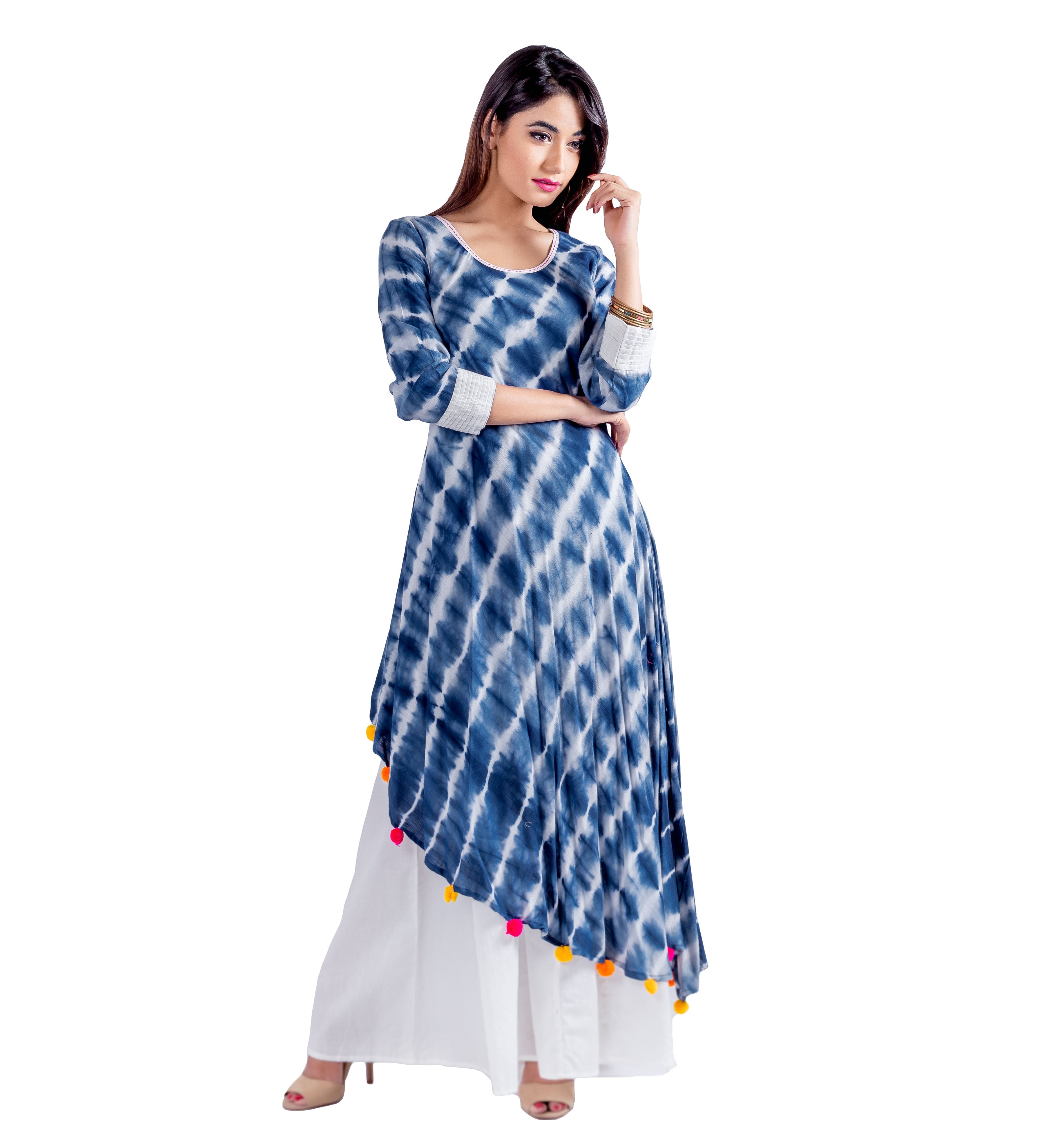Model wears blue and white tie-dye asymmetric kurta with colorful pom-poms over white palazzo pants.
