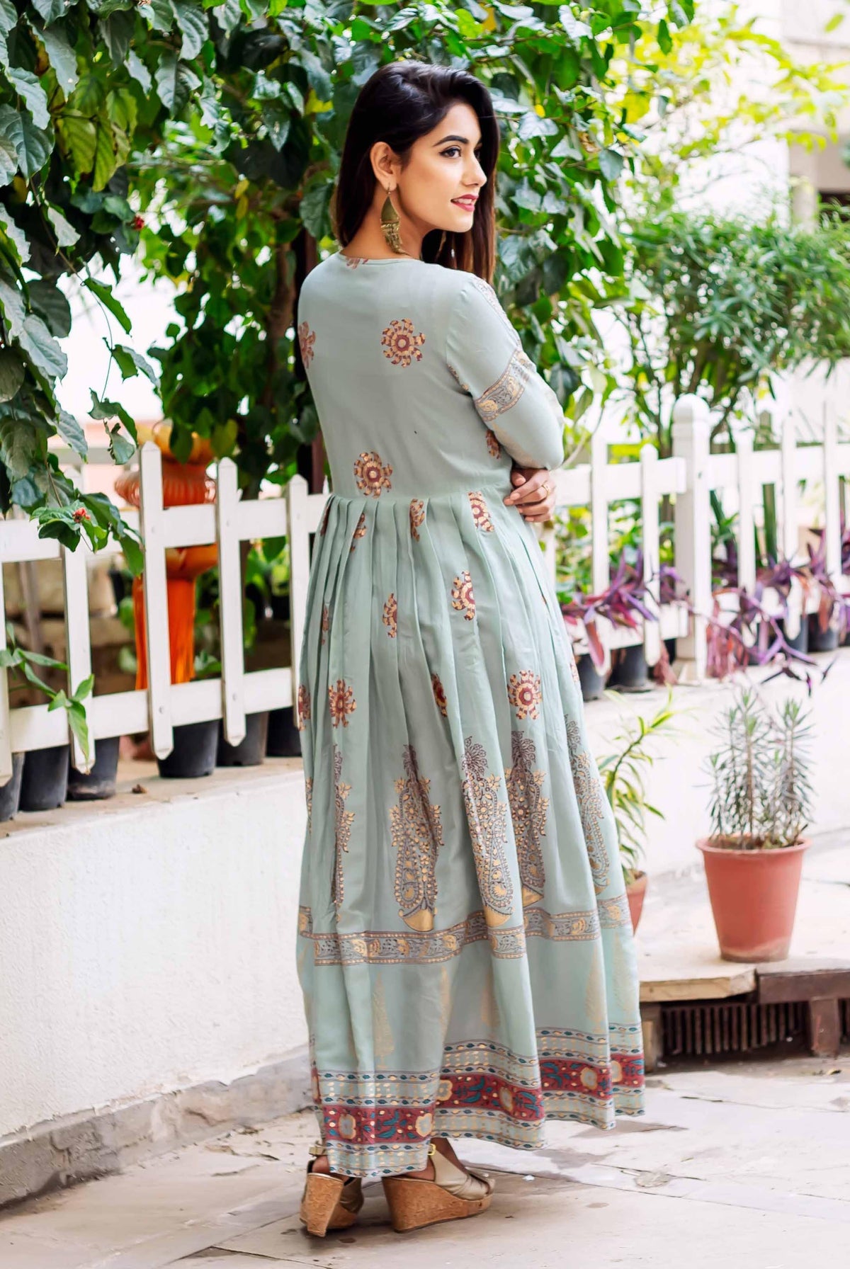 Back-side view of model in full-length sage green Indowestern dress with ethnic block prints.