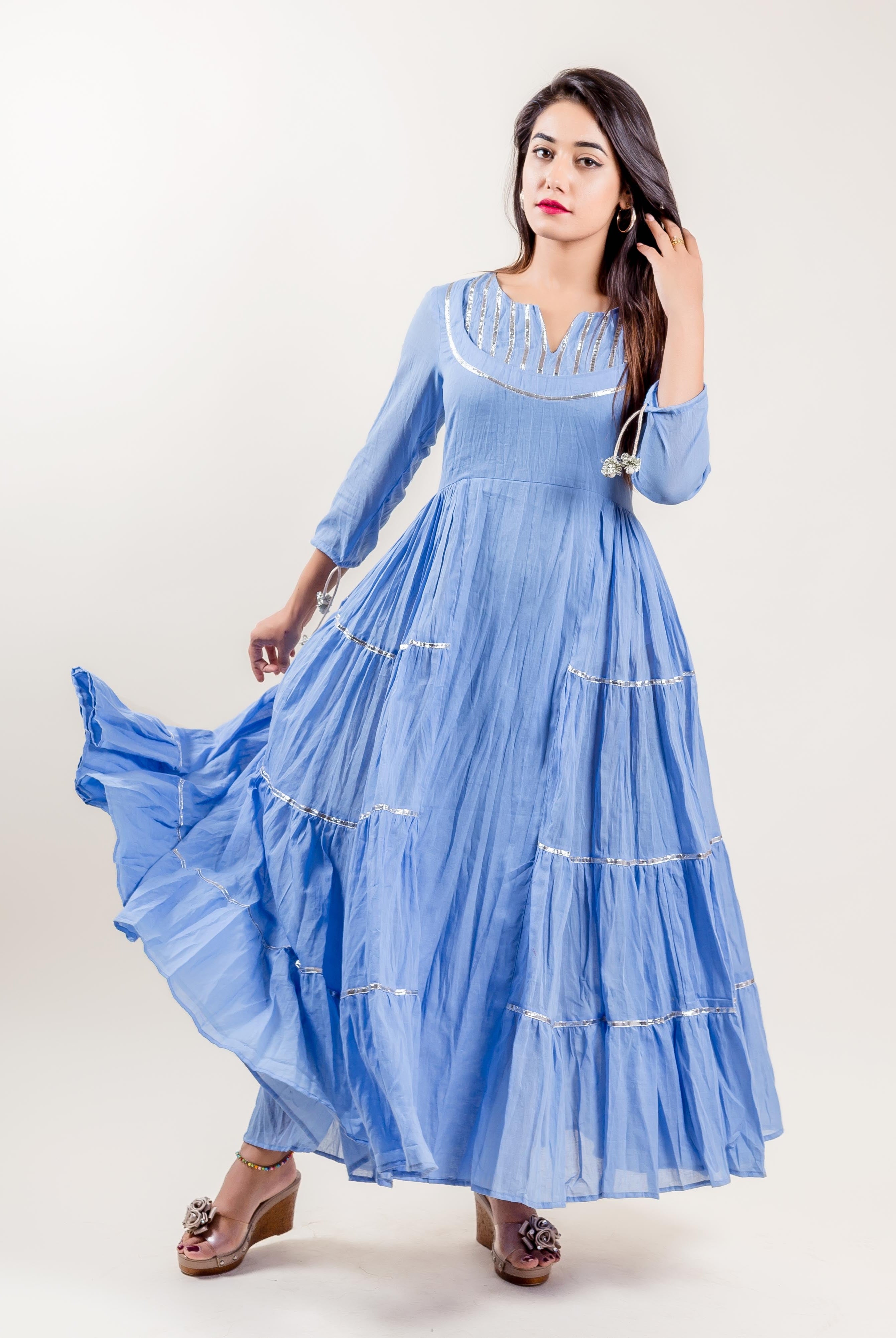 Front view of a woman in a blue tiered gown dress with silver decorative trim.