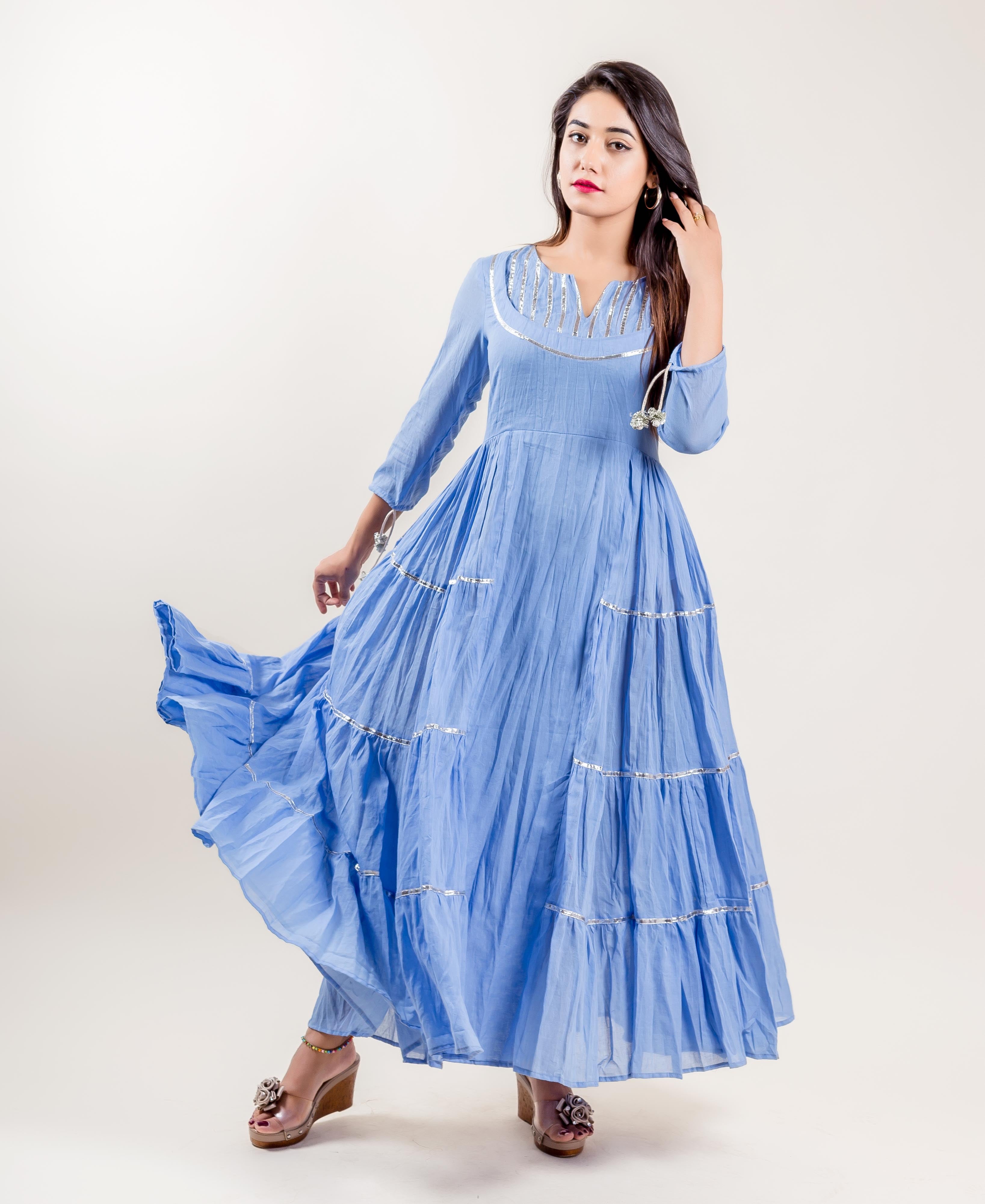 Front view of a woman in a blue tiered gown dress with silver decorative trim.
