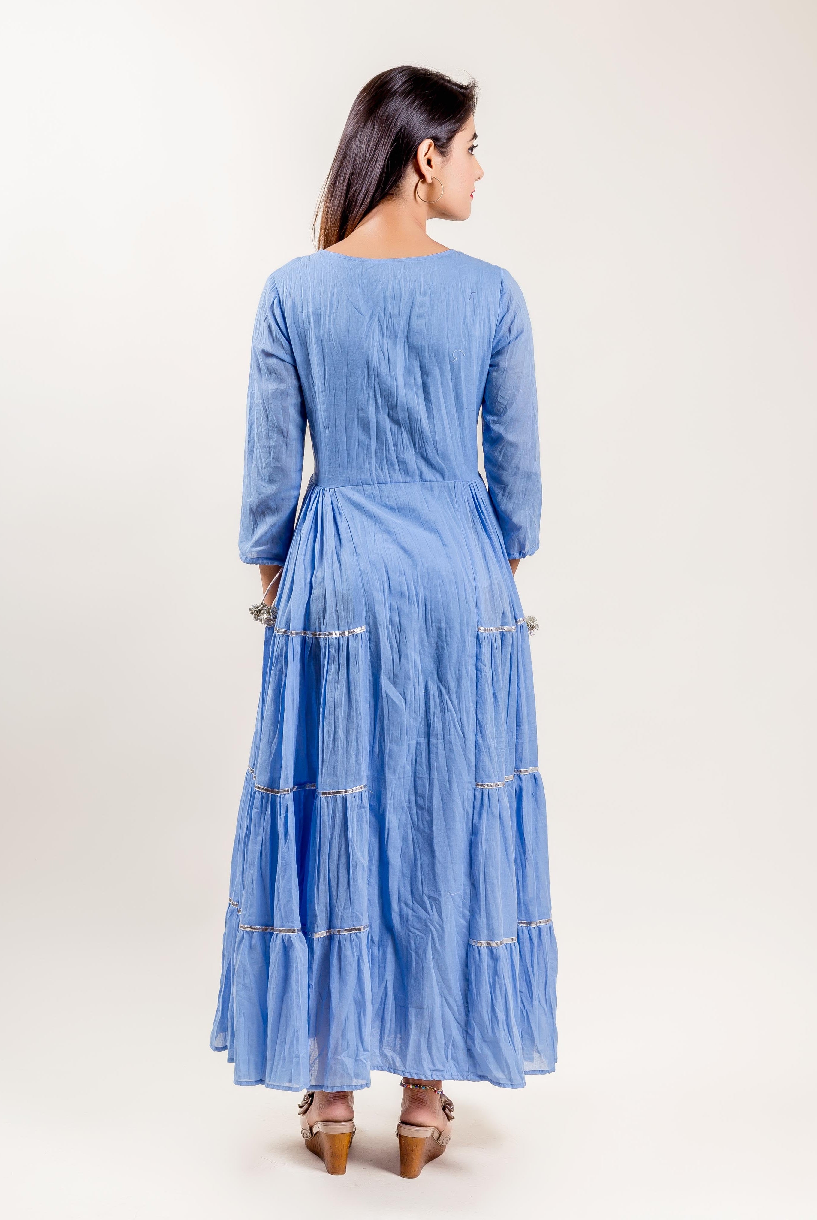 Back view of a model in a blue cotton tiered gown dress with silver trims.