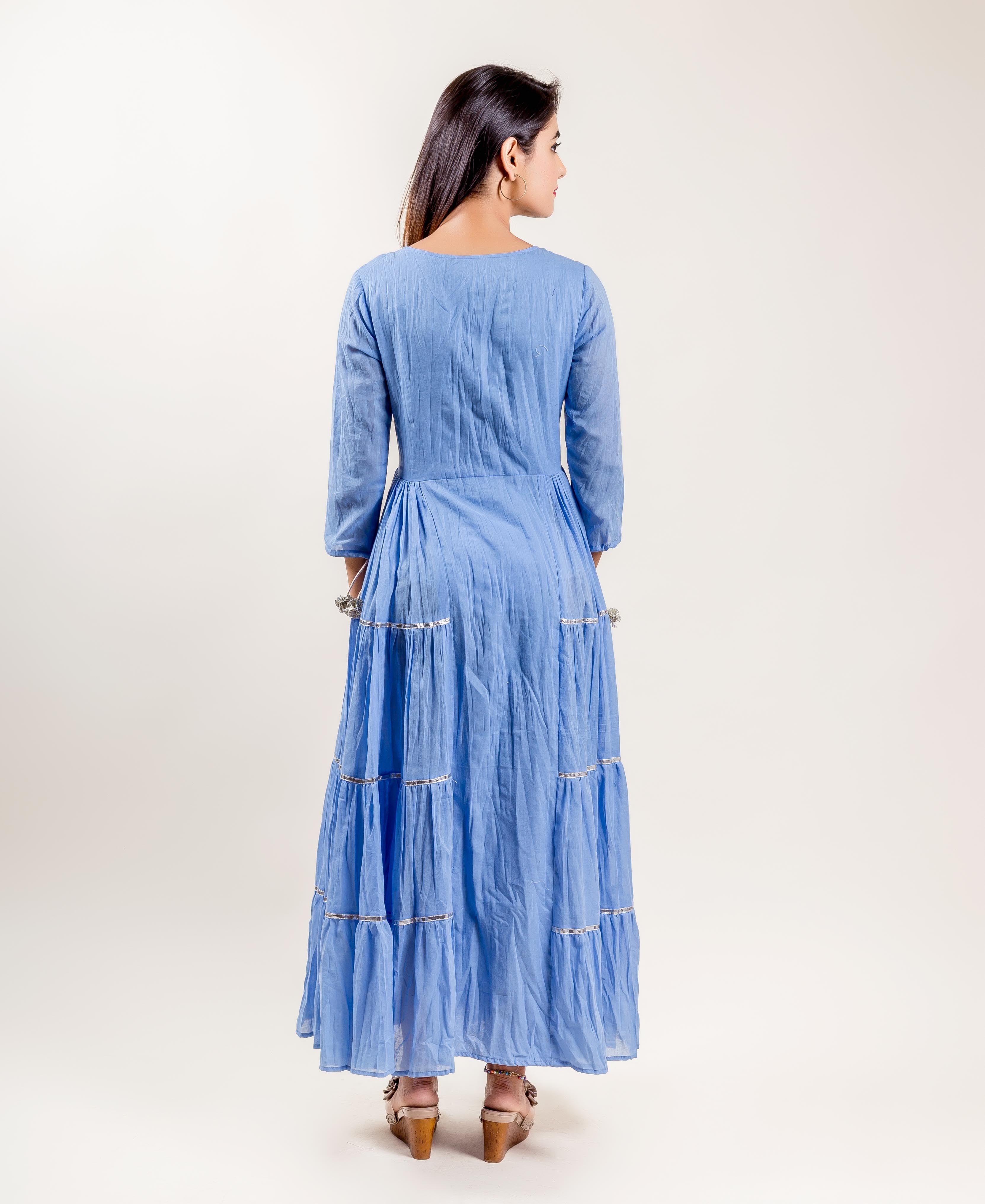 Back view of a model in a blue cotton tiered gown dress with silver trims.