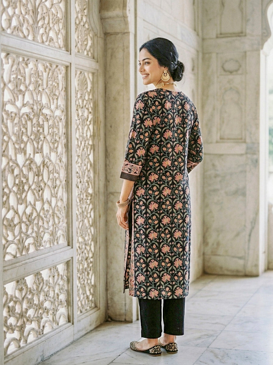 Side view of model wearing black floral hand block printed kurta and black pants.
