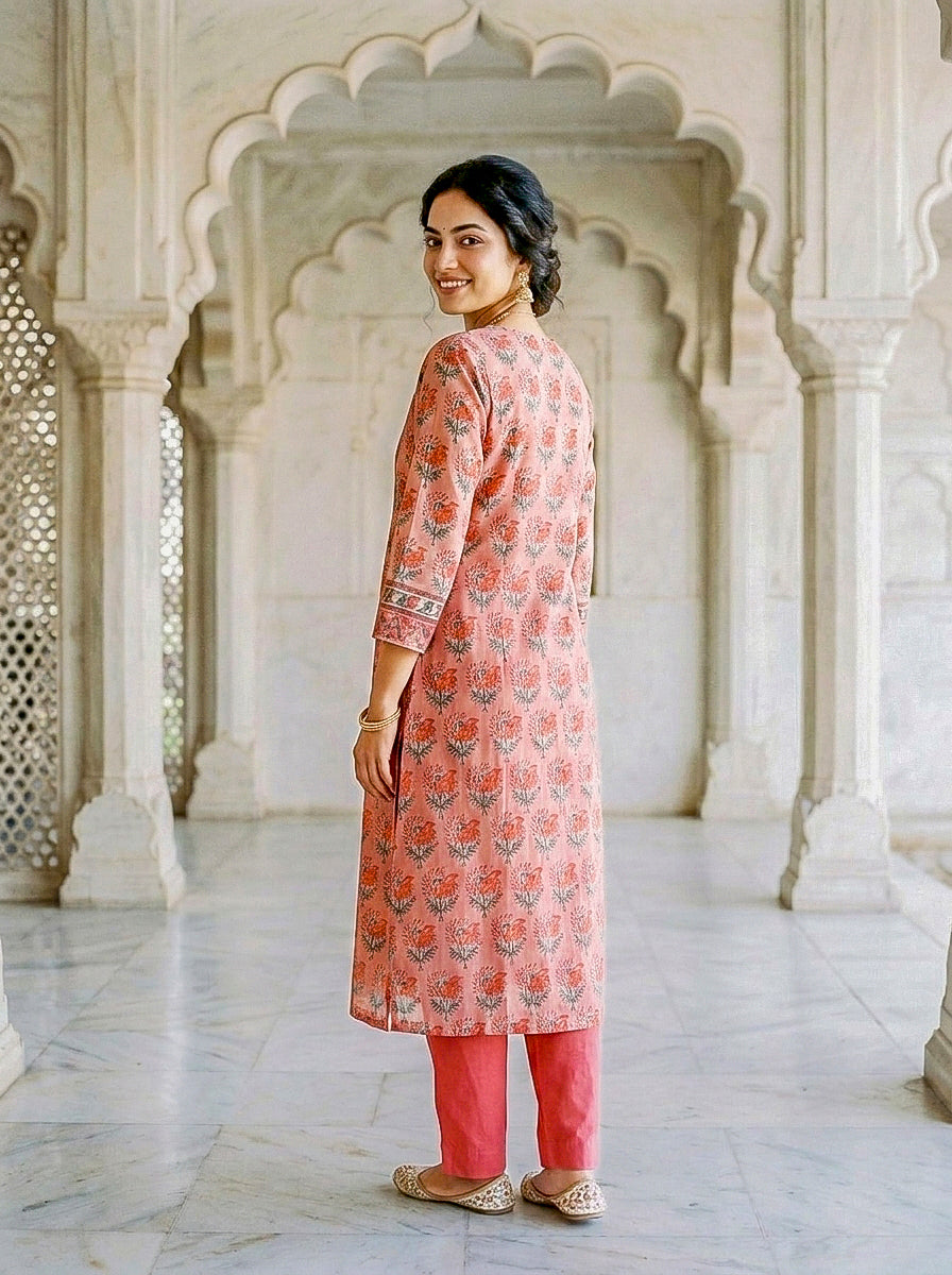 Side-back view of model in coral hand block print kurta with floral motifs and coral pants.